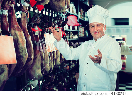 Portrait of mature shop man offering Spanish jamon 41882953