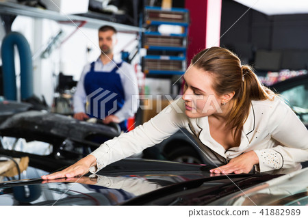 Female client closely examining car body after repainting in auto workshop Female client closely examining car body after repainting in auto workshop 41882989