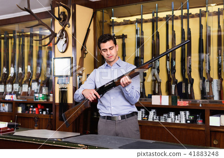 Handsome adult male owner of hunting shop offering rifle Handsome adult male owner of hunting shop offering rifle 41883248