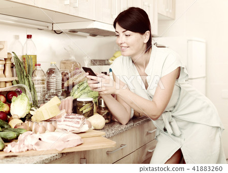 Cheerful woman is chatting by phone in time cooking on the kitchen Cheerful woman is chatting by phone in time cooking on the kitchen 41883260