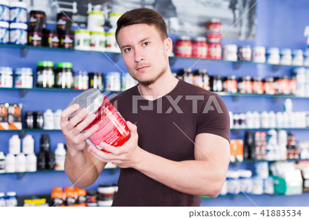 Young muscular guy choosing sport nutrition products in shop Young muscular guy choosing sport nutrition products in shop 41883534