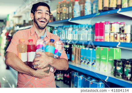 Portrait of man customer who is standing with drinks in supermarket. Portrait of man customer who is standing with drinks in supermarket. 41884134