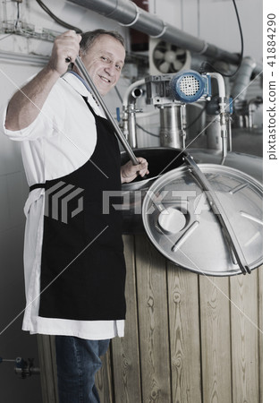 Adult brewer is standing with tube near reservoir for beer 41884290