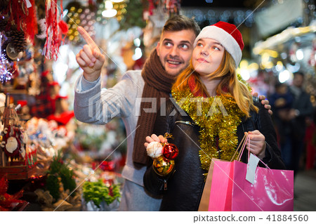 Young couple in hat at Christmas fair, man points to toys Young couple in hat at Christmas fair, man points to toys 41884560