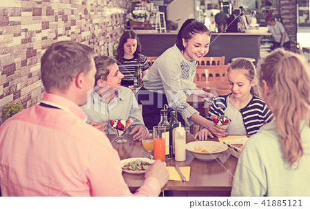 Young brunette waitress serving positive family in family cafe Young brunette waitress serving positive family in family cafe 41885121