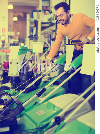attentive guy deciding on best lawnmower in garden equipment shop 41886475