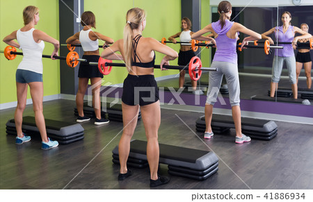 Group of smiling girls in sportwear performing weight lifting Group of smiling girls in sportwear performing weight lifting 41886934