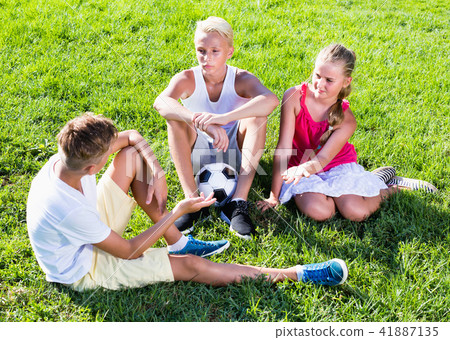 Three smiling kids with ball resting on grass on summer day Three smiling kids with ball resting on grass on summer day 41887135