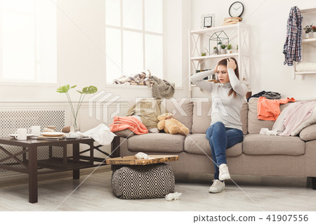 Desperate woman sitting on sofa in messy room 41907556