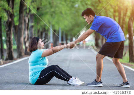 Asian man pulling hand of fat woman who tired and sitting on ground Asian man pulling hand of fat woman who tired and sitting on ground 41916378