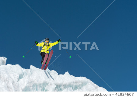 A jumping skier jumping from a glacier against a blue sky high in the mountains. Professional skiing 41924607