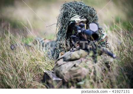 Sniper laying on grass looking through scope. 41927131