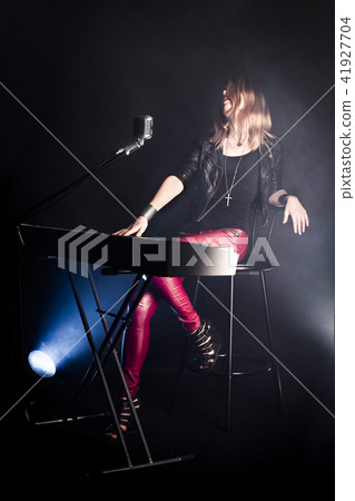 Blonde girl musician pianist plays perform on white digital piano, sits on chair, sings into retro Blonde girl musician pianist plays perform on white digital piano, sits on chair, sings into retro 41927704