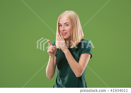 The young woman whispering a secret behind her hand over green background The young woman whispering a secret behind her hand over green background 41934011