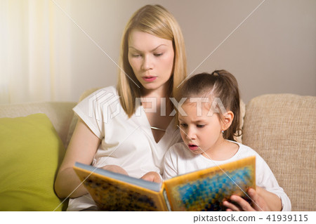 Pretty beautiful mother and her young daughter are reading a book. 41939115