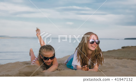 Two teenage children are sitting on the beach. 41947132