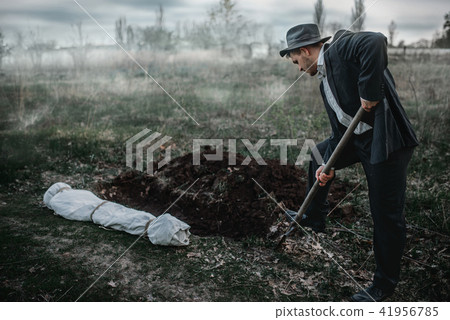 Killer is digging a grave for the victim in forest 41956785