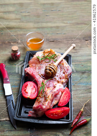 Raw steaks and frying pans with seasoning, garnishes and ingredients on a dark rustic background Raw steaks and frying pans with seasoning, garnishes and ingredients on a dark rustic background 41962579