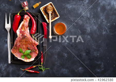 Raw steaks and frying pans with seasoning, garnishes and ingredients on a dark rustic background Raw steaks and frying pans with seasoning, garnishes and ingredients on a dark rustic background 41962580