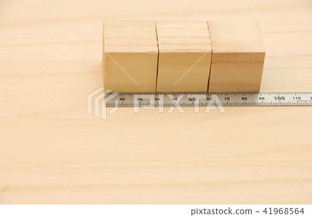 A cube wood and a metal ruler (straight scale) placed on a wooden board. 41968564
