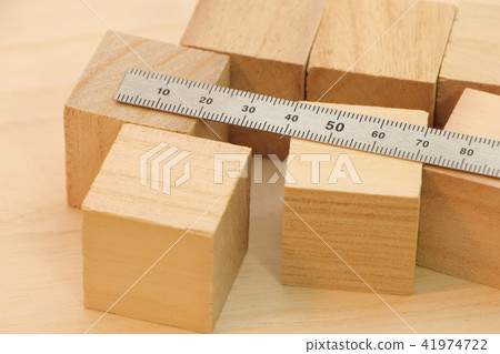 A cube wood and a metal ruler (straight scale) placed on a wooden board. A cube wood and a metal ruler (straight scale) placed on a wooden board. 41974722