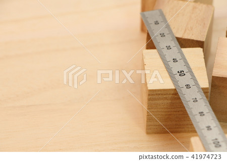 A cube wood and a metal ruler (straight scale) placed on a wooden board. 41974723