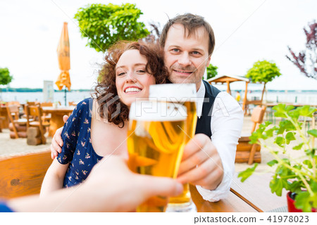 Couple toasting toward friends in beer garden pub Couple toasting toward friends in beer garden pub 41978023