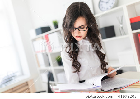 Beautiful young girl stands in the office thumbs a folder with documents. 41978203