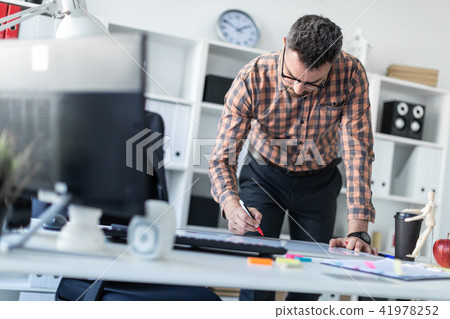 A man in the office is standing near the table and draws a marker on the magnetic board. 41978252