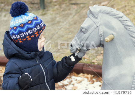 Two year toddler playing with a toy horse. Kid feeding wooden horse 41979755