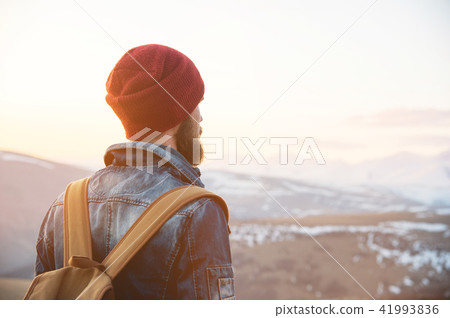 Bearded tourist hipster man in a hat with a backpack stand back on a roadside bump and watching the Bearded tourist hipster man in a hat with a backpack stand back on a roadside bump and watching the 41993836