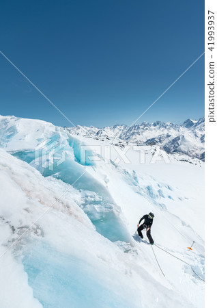 A professional mountaineer in a helmet and ski mask on insurance makes a nick-hole in the glacier 41993937