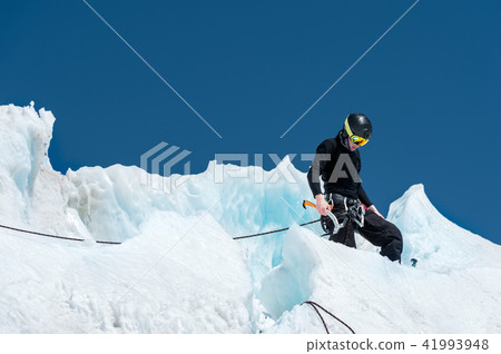 A professional mountaineer in a helmet and ski mask on the insurance does notch the ice ax in the A professional mountaineer in a helmet and ski mask on the insurance does notch the ice ax in the 41993948