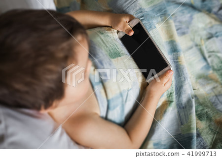 small boy holding touching phone lying on the bed in morning small boy holding touching phone lying on the bed in morning 41999713