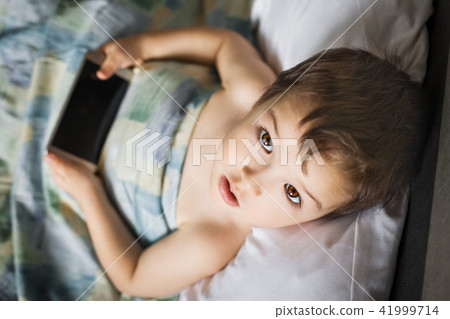 young boy holding smartphone lying on the bed in morning young boy holding smartphone lying on the bed in morning 41999714