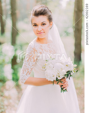 Outdoor portrait of the charming bride holding the wedding bouquet of peonies. 42002169