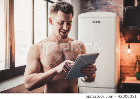 Bare-chested Young Man with Tablet in Kitchen. Bare-chested Young Man with Tablet in Kitchen. 42006051