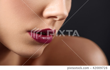 Cropped close up of woman's lips covered with dark lipstick. 42009728