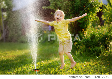 Funny little boy playing with garden sprinkler in sunny backyard Funny little boy playing with garden sprinkler in sunny backyard 42012249
