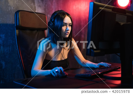 A cute female gamer girl sits in a cozy room behind a computer and plays games. Woman live streaming 42015978