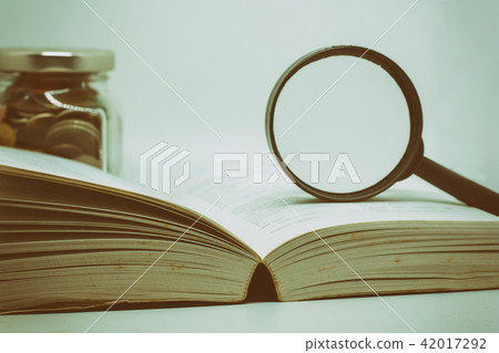 Magnifying glass on opened book with blurred coins 42017292