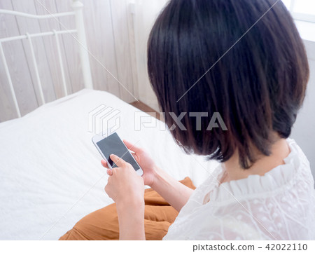 asian woman on bed checking smartphone  42022110