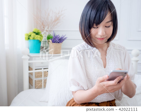 asian woman on bed checking smartphone  42022111
