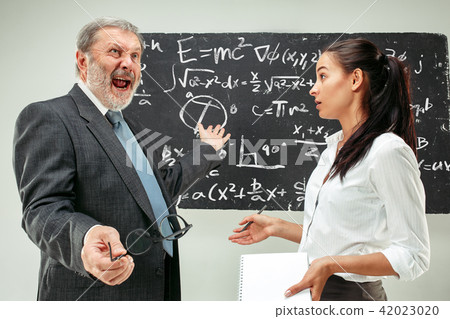 Male professor and young woman against chalkboard in classroom Male professor and young woman against chalkboard in classroom 42023020