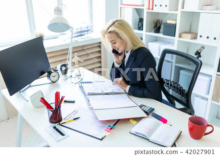 Young girl sitting at desk in office, talking on phone and looking at documents. Young girl sitting at desk in office, talking on phone and looking at documents. 42027901