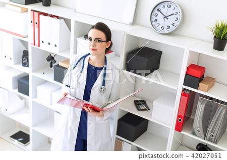 A beautiful young girl in a white robe is standing near the shelter and flips through a red folder 42027951