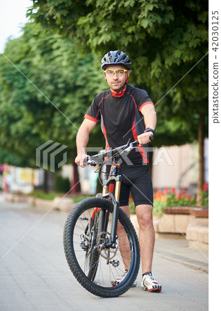 Cyclist posing near bike on city street Cyclist posing near bike on city street 42030125