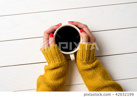 Female hands in warm sweater holding cup of coffee Female hands in warm sweater holding cup of coffee 42032199