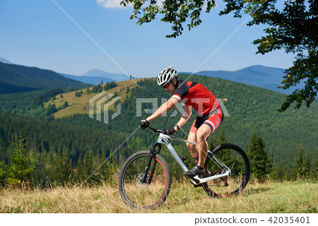 Strong athletic sportsman in professional sportswear cycling a bicycle in high grass Strong athletic sportsman in professional sportswear cycling a bicycle in high grass 42035401