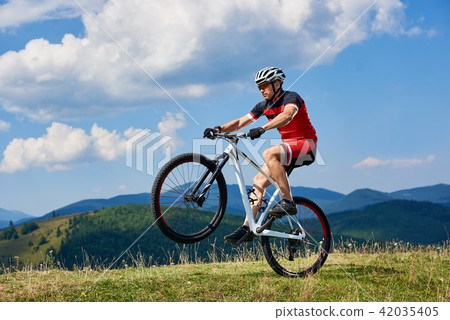 Cyclist riding cross country bike, turning on one wheel of bicycle on mountain hill 42035405